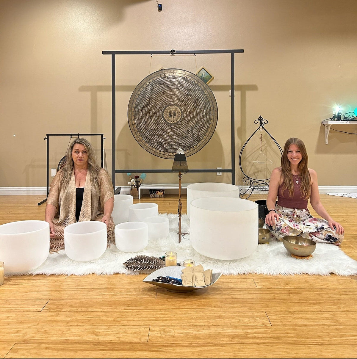 Two women in a room with gongs and other instruments on a wooden floor.